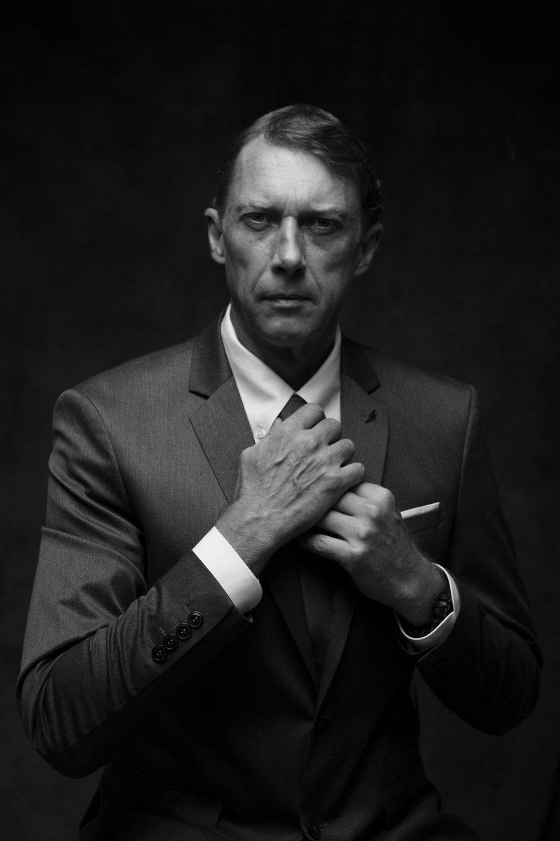 Black-and-white portrait of a man adjusting the lapel of his suit